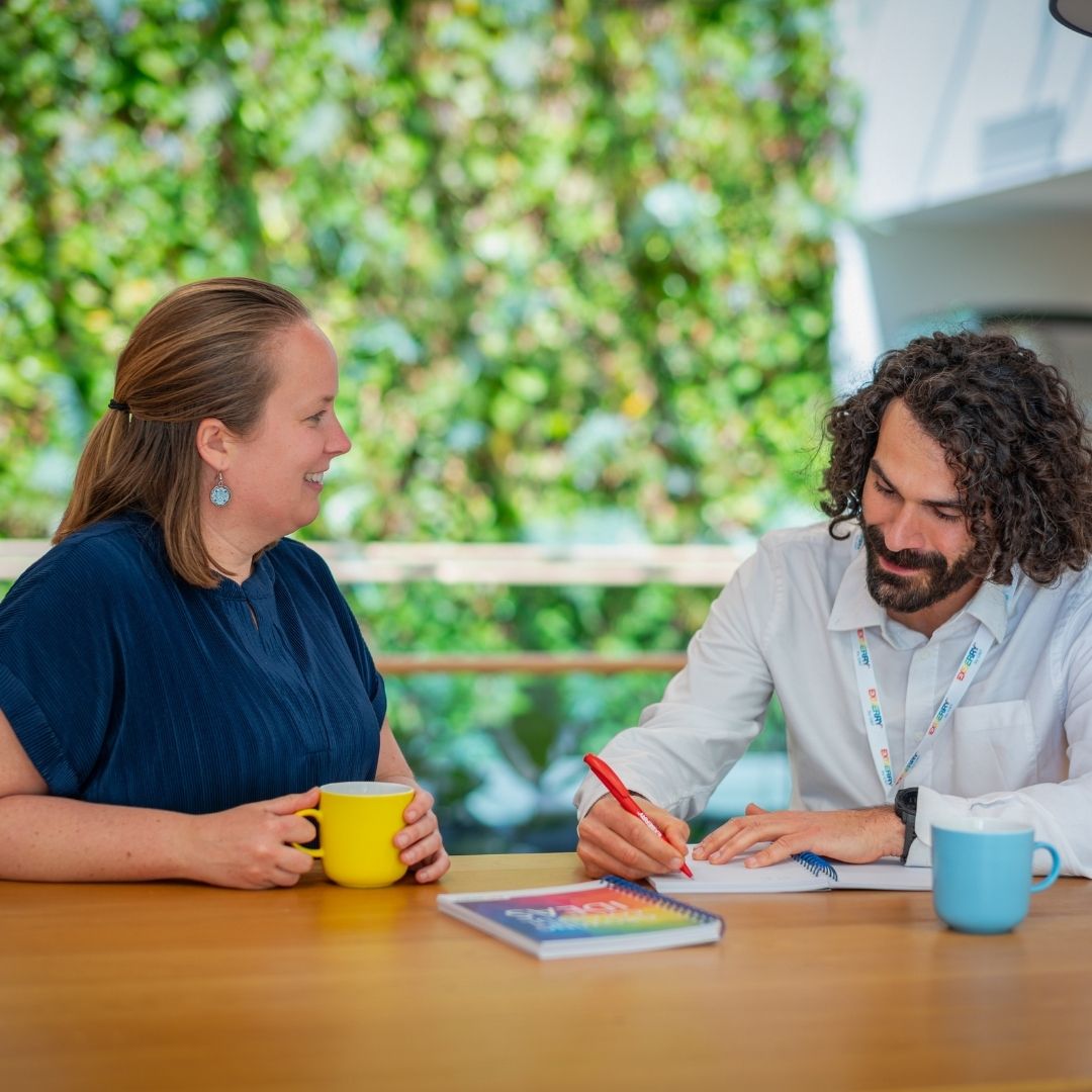 Man and woman having a conversation at a table with a green background