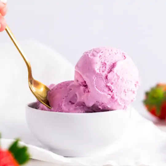 Scoops of ice cream with pink food colors in a bowl with strawberries and a golden spoon